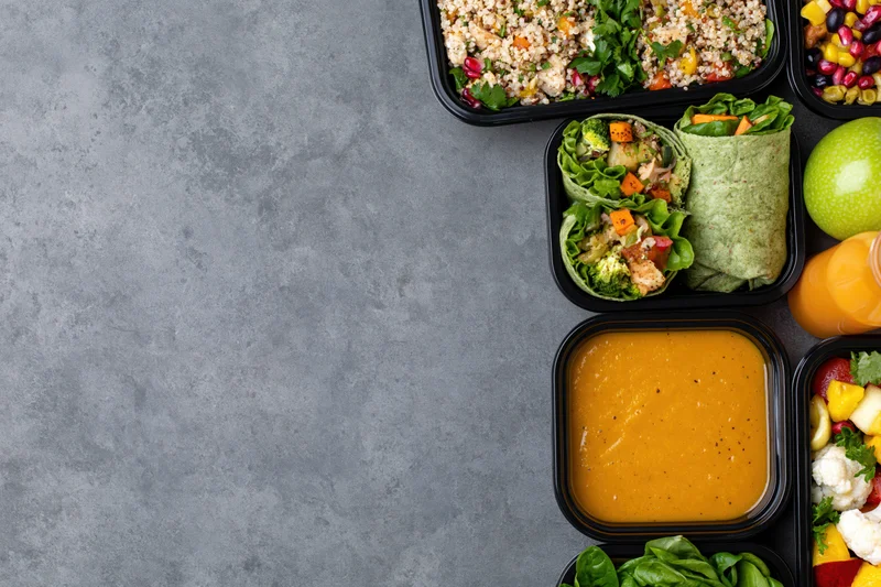 Healthy meal prep containers arranged along the right side of a gray textured surface with copyspace on the left
