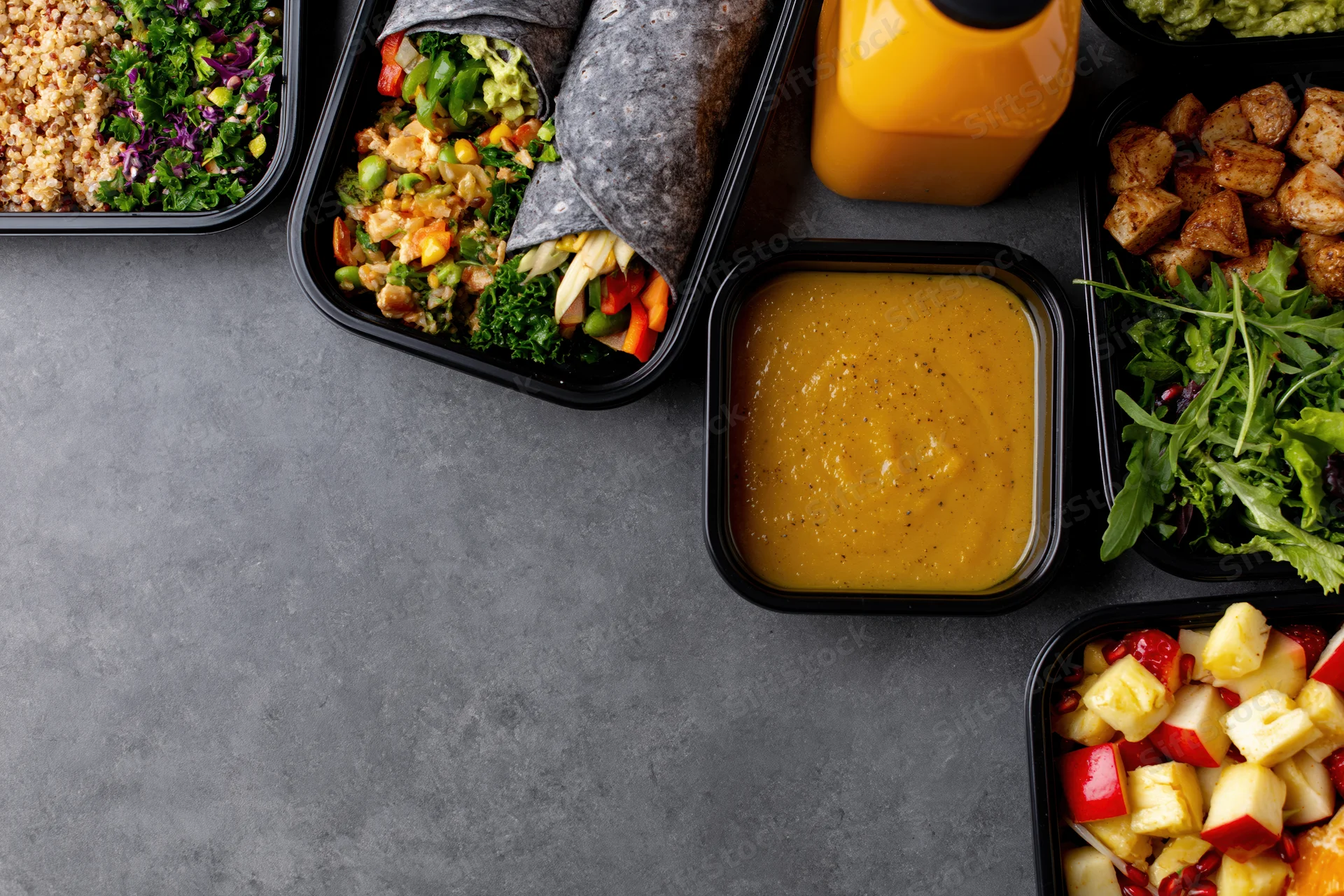 Assorted healthy meal prep containers arranged along the right side of a dark gray surface with copyspace on the left