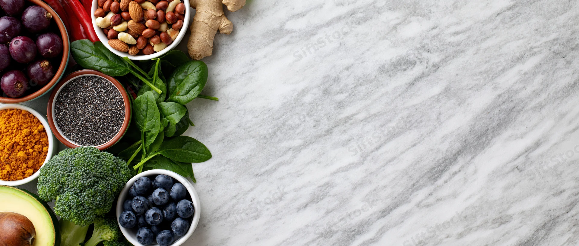 Assorted healthy whole foods arranged along the left edge of a marble countertop with copyspace on the right