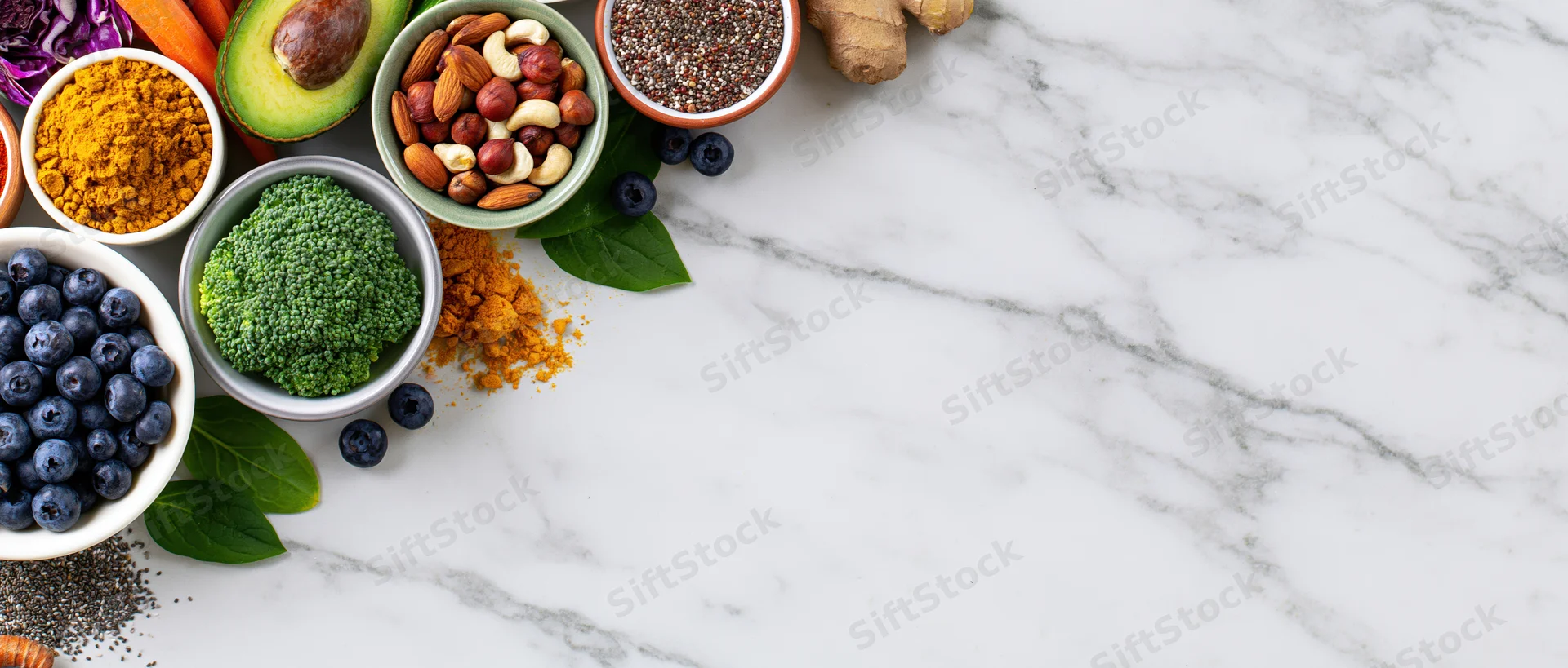 Assorted healthy whole foods arranged along the left edge of a marble countertop with copyspace on the right