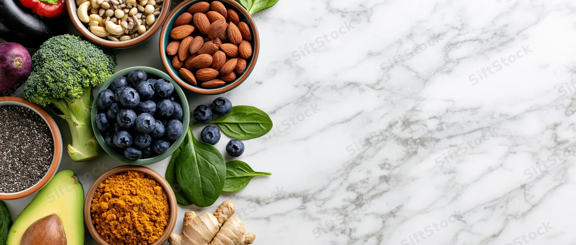 Assorted healthy whole foods arranged along the left edge of a marble countertop with copyspace on the right