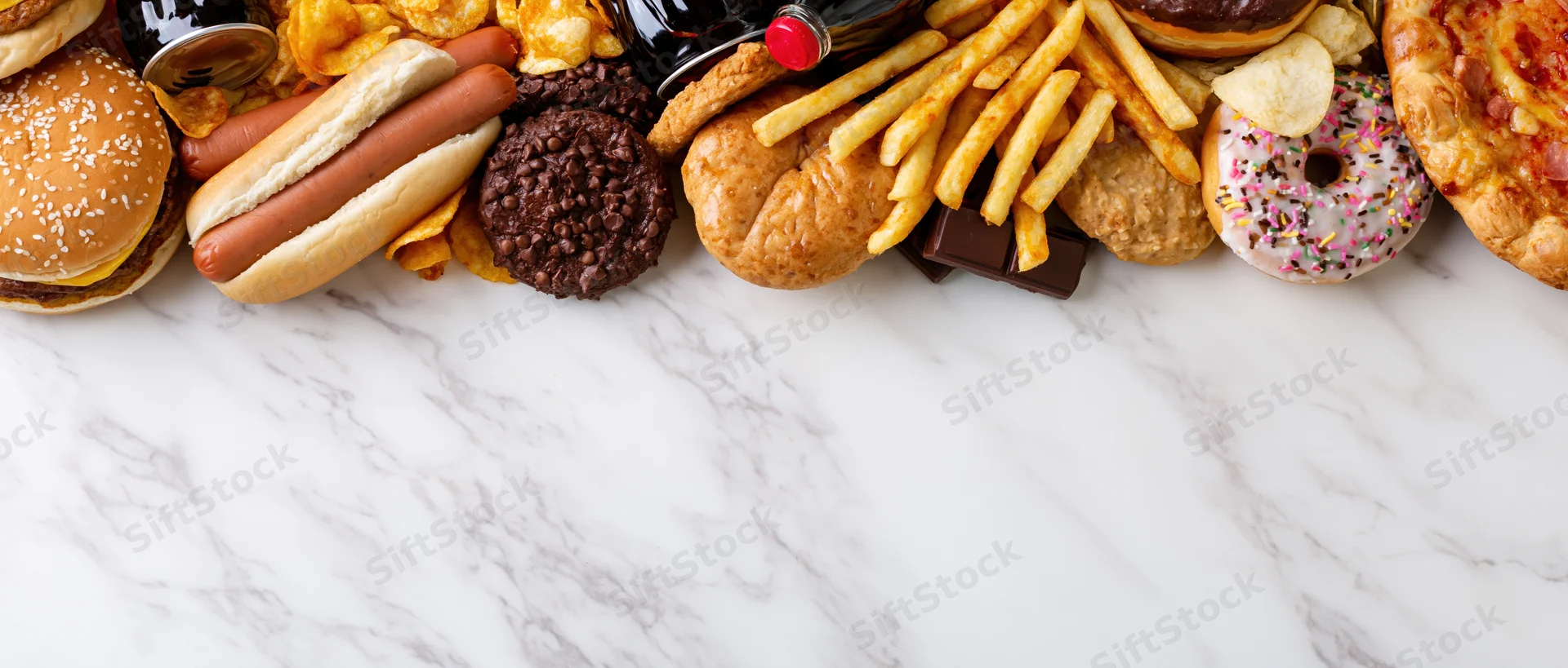 Assorted junk food and fast food items arranged in a dense horizontal row along the top of a marble countertop with copyspace below