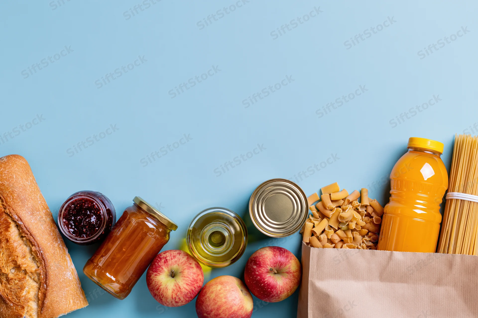 Assorted pantry staples and grocery items arranged along the bottom of a blue surface with copyspace above