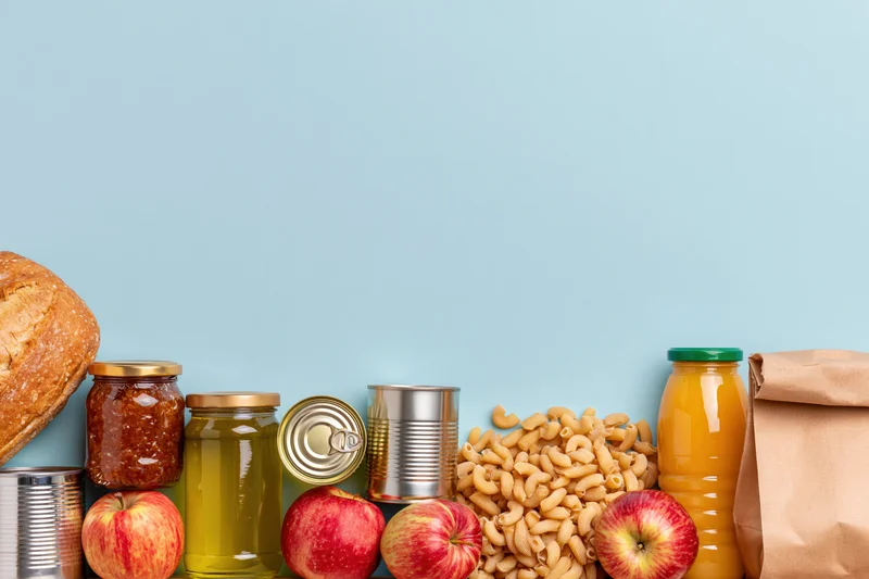 Assorted pantry staples and grocery items arranged along the bottom of a light blue background with copyspace above