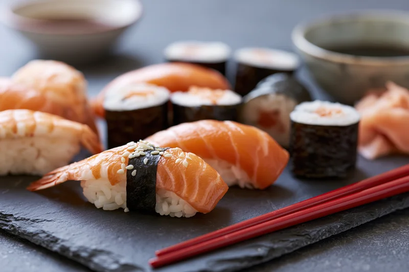 Assorted sushi nigiri and rolls with chopsticks on dark slate plate