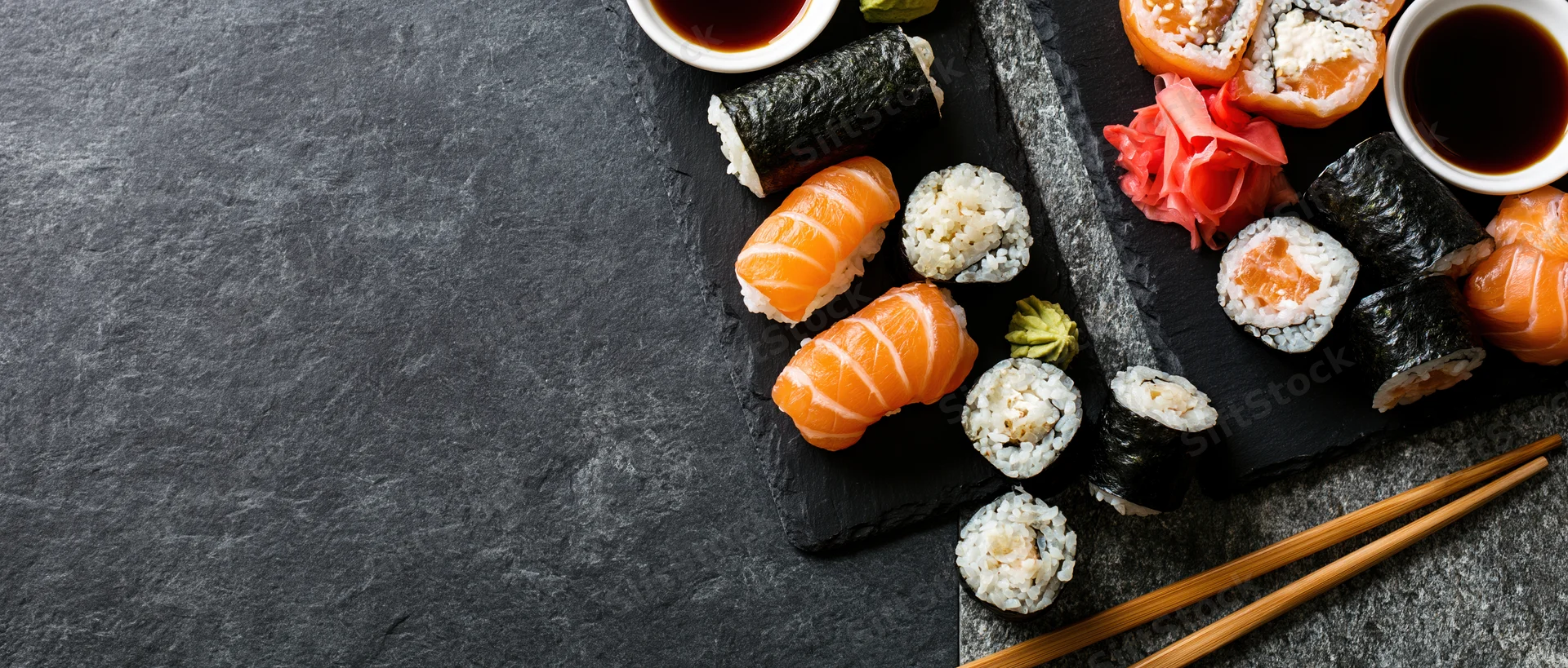 Assorted sushi pieces with soy sauce and wasabi arranged on black slate boards with chopsticks and copyspace