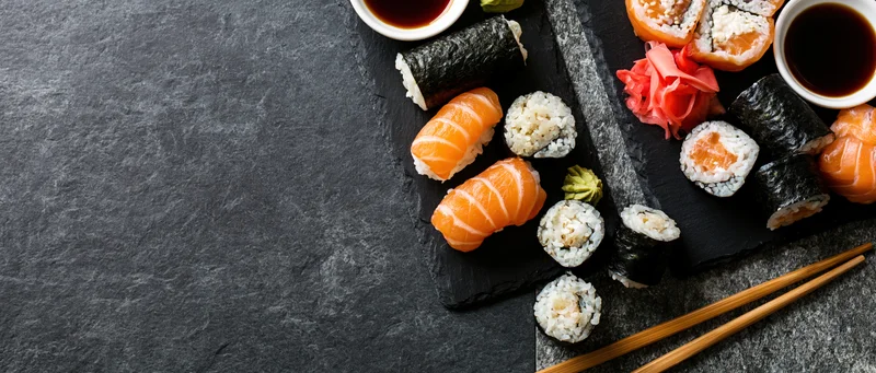 Assorted sushi pieces with soy sauce and wasabi arranged on black slate boards with chopsticks and copyspace
