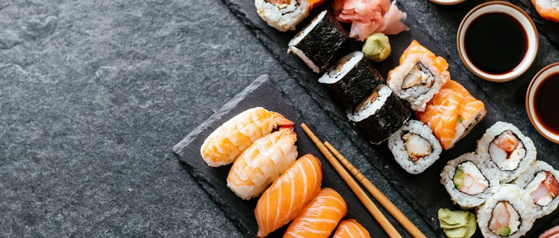 Assorted sushi pieces with chopsticks and soy sauce arranged on black slate boards on a dark stone surface