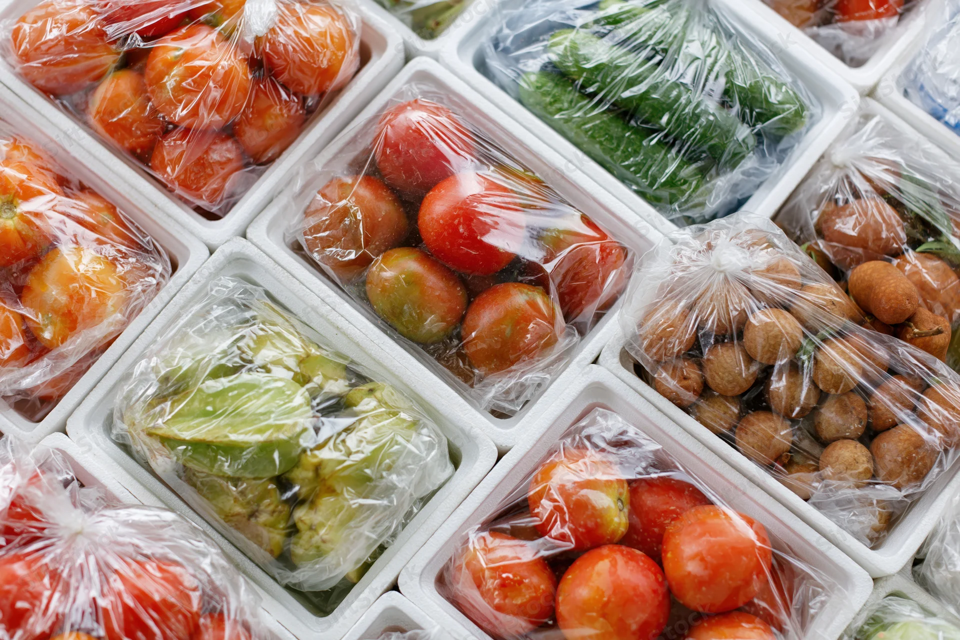 Assorted tropical fruits and vegetables packed in plastic-wrapped containers in a grocery store display