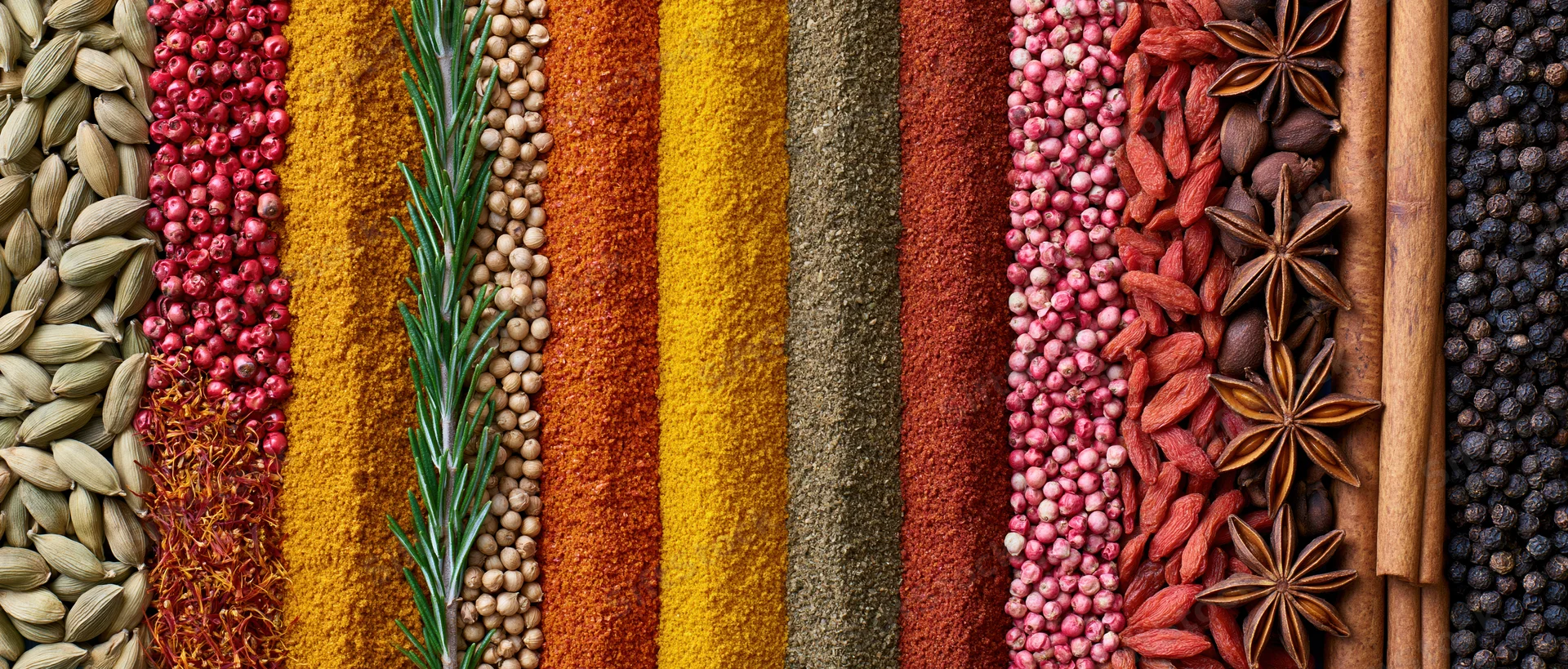 Vertical arrangement of whole and ground spices in colorful stripes across a flat surface