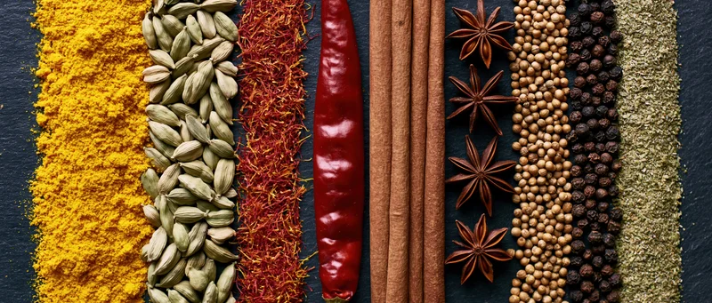 Vertical arrangement of assorted whole and ground spices on dark slate surface