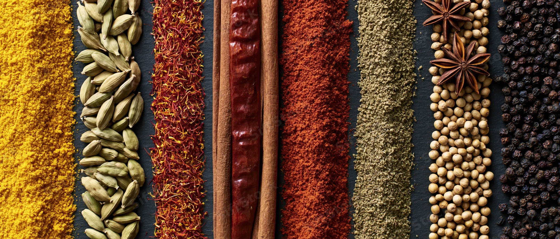 Vertical rows of assorted whole and ground spices arranged on dark surface