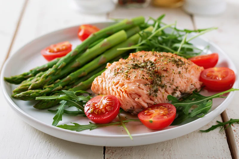 Baked salmon fillet with asparagus and cherry tomatoes on a white plate on a wooden table