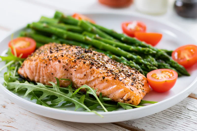 Baked salmon fillet with asparagus and cherry tomatoes on a white plate over wooden table