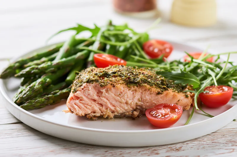 Baked salmon fillet with herb crust served on a white plate with asparagus and cherry tomatoes