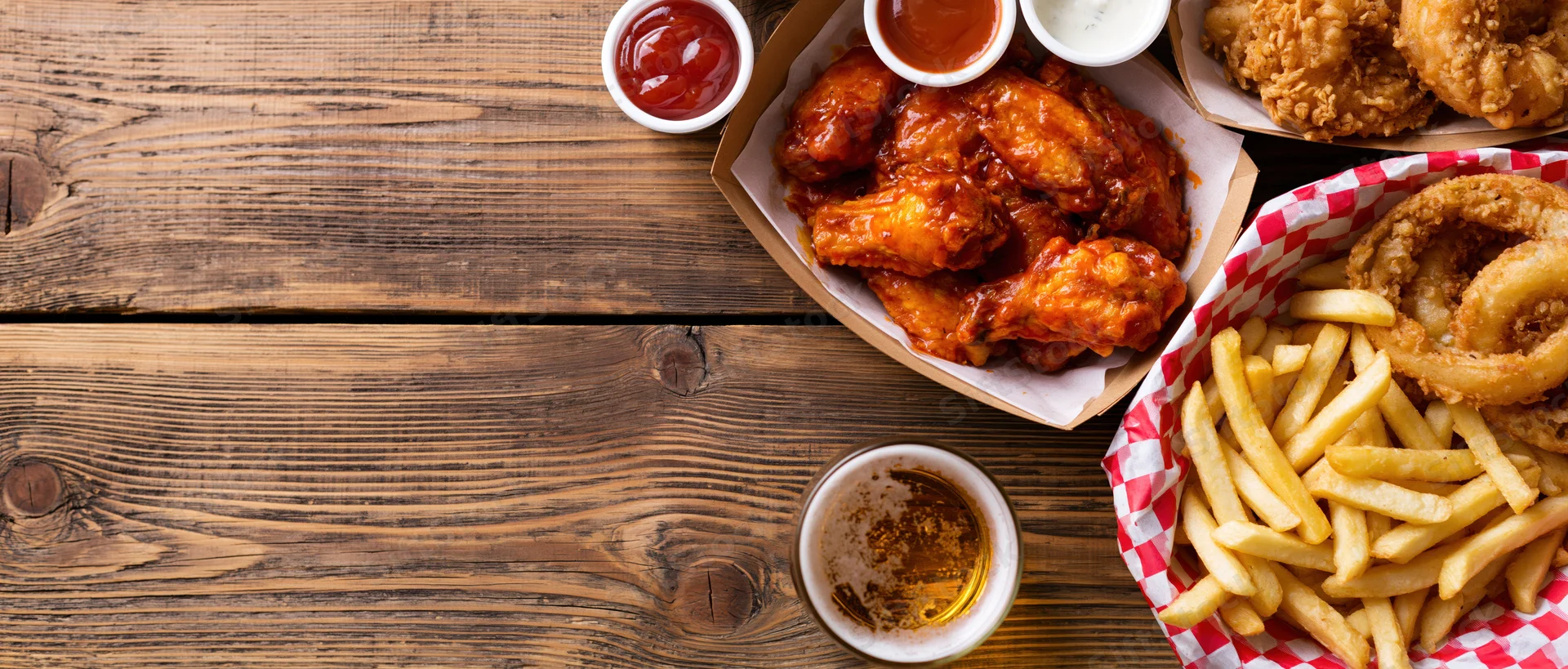 Buffalo chicken wings and fries on a worn wooden table with beer and dipping sauces