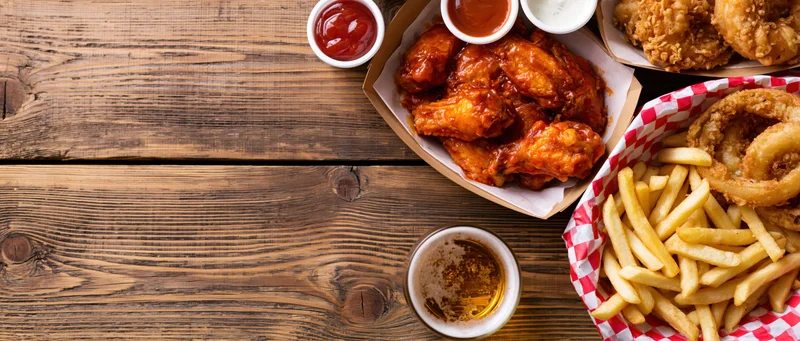 Buffalo chicken wings and fries on a worn wooden table with beer and dipping sauces