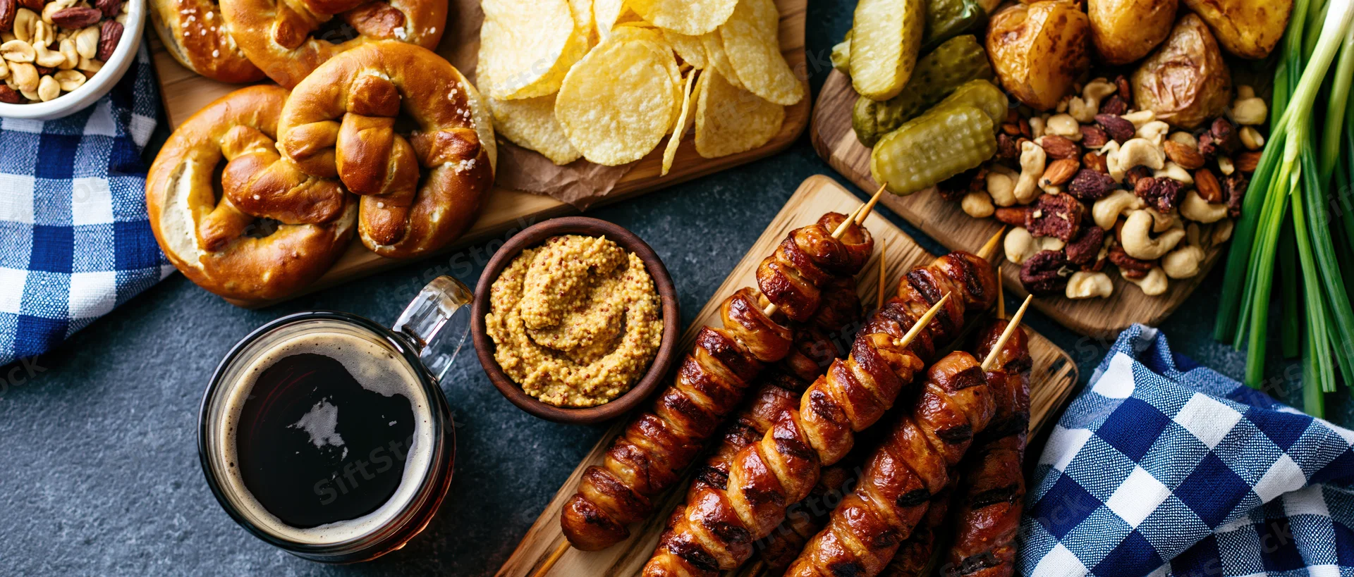Bavarian oktoberfest food spread with pretzels, sausages, beer and mustard on dark grey surface
