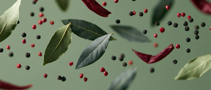 Bay leaves, red chili peppers, and peppercorns floating in midair against a muted green background