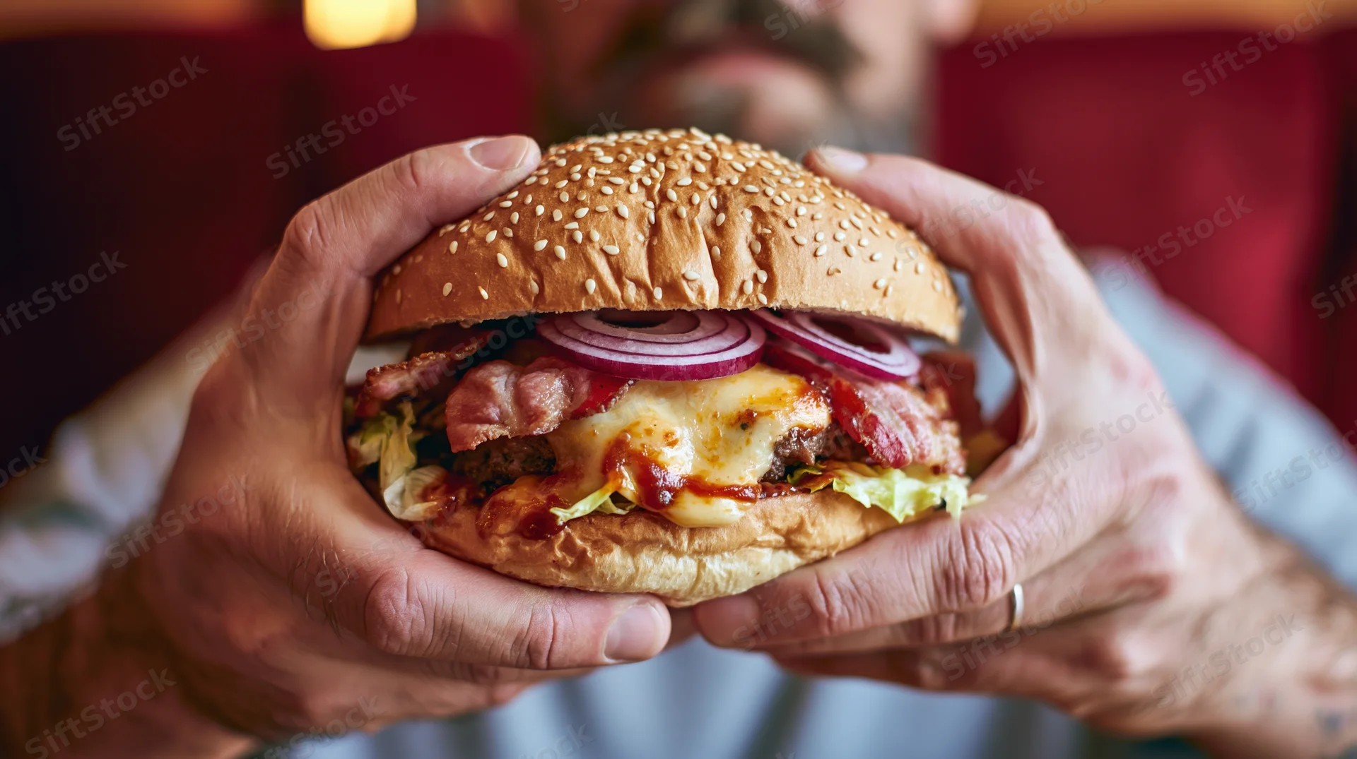 Man holding large loaded burger with both hands in closeup view