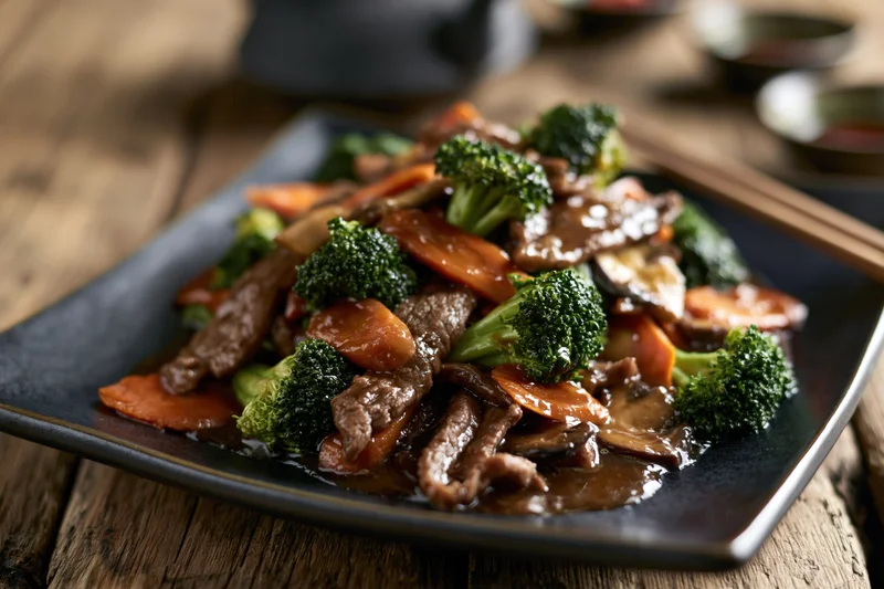Beef and vegetable stir-fry served on a dark square ceramic plate on a wooden table