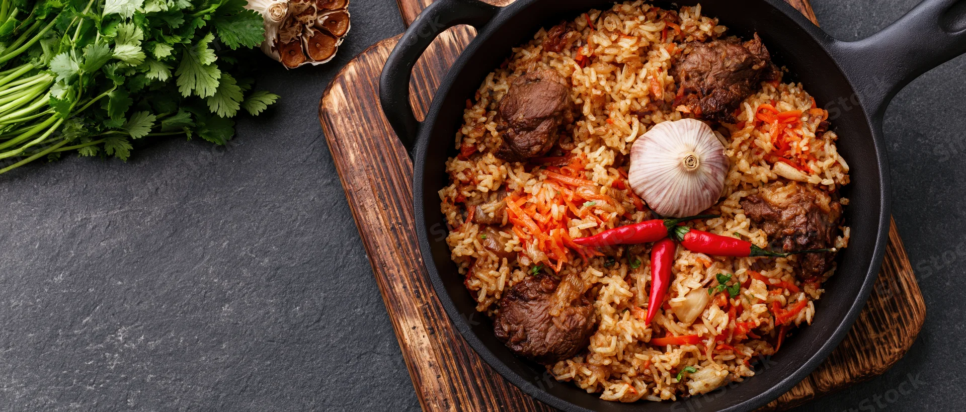 Central asian plov rice pilaf with meat and vegetables in a cast iron pan on a wooden board