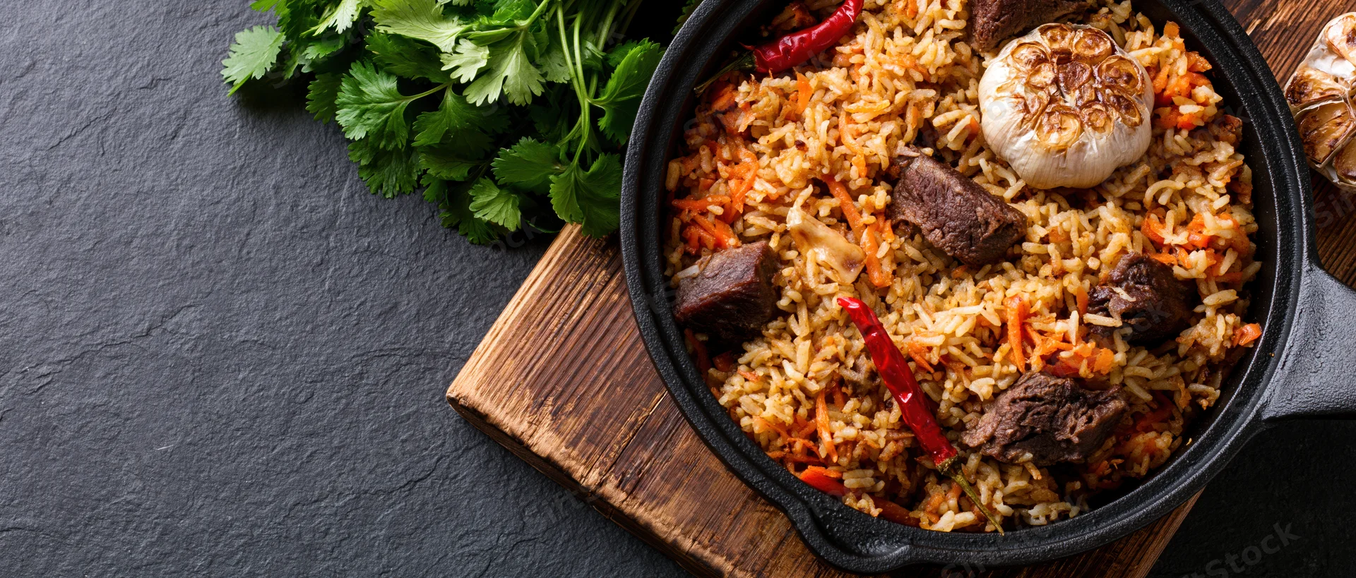 Central asian plov rice pilaf with beef and vegetables in a cast iron pan on a wooden board