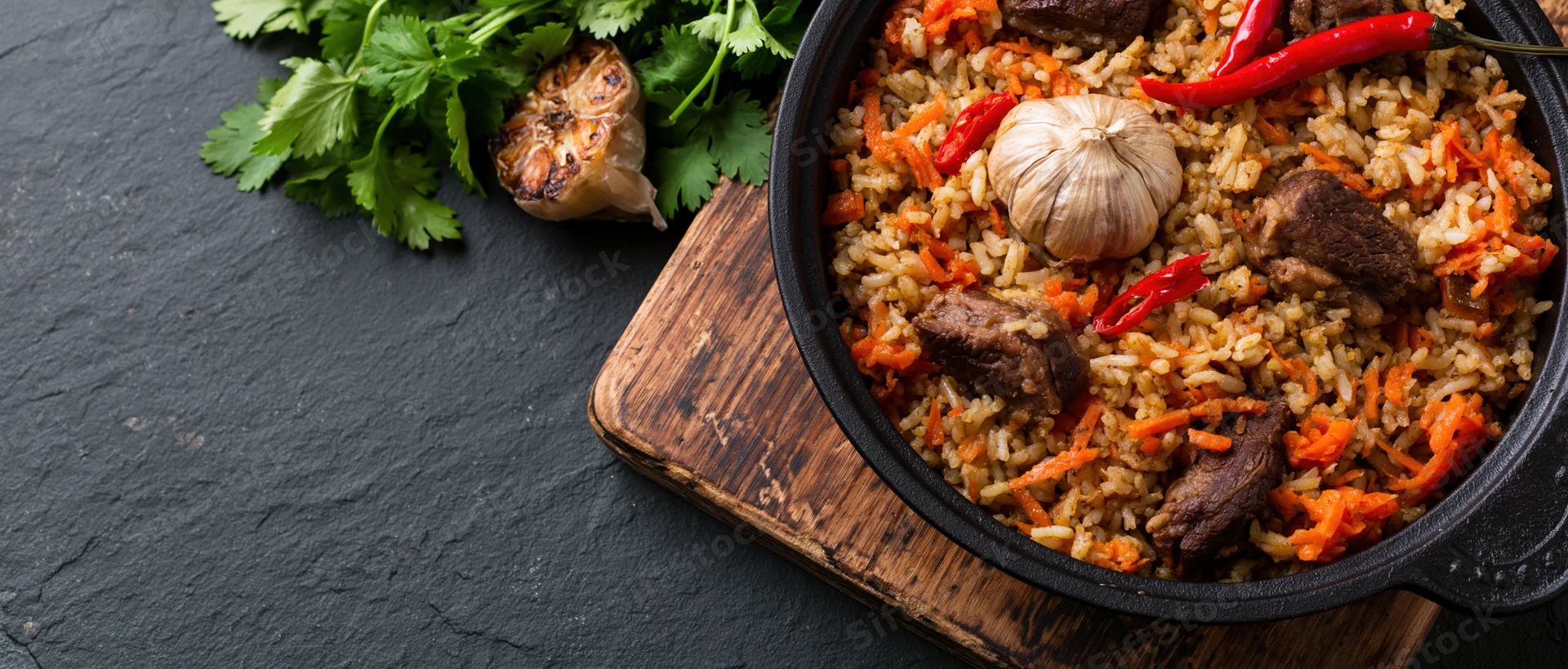 Central asian plov rice pilaf with meat and vegetables in a black cast iron pan on a wooden board