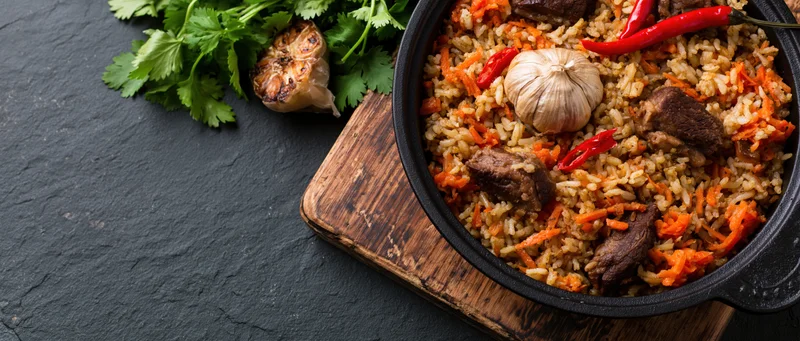 Central asian plov rice pilaf with meat and vegetables in a black cast iron pan on a wooden board