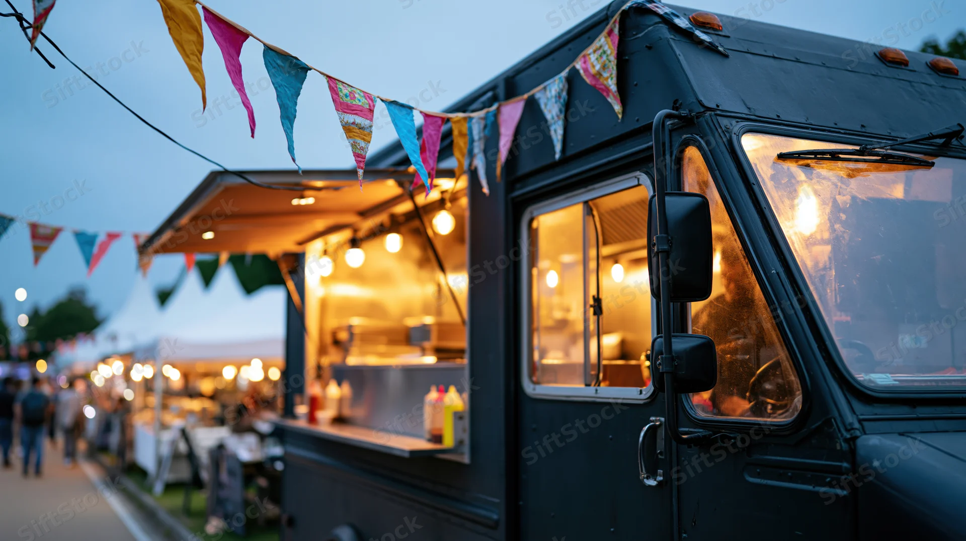 Black food truck with open service window and warm interior lights at evening market