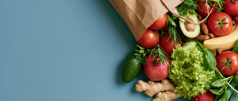 Brown paper grocery bag tipped on its side spilling fresh produce onto a blue surface