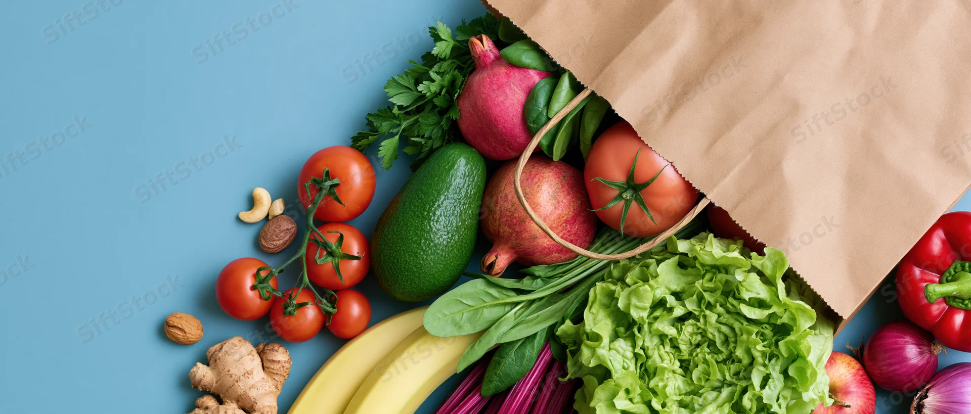 Brown paper grocery bag tipped over spilling fresh vegetables and fruits on blue surface
