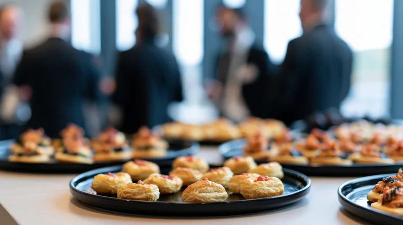 Small appetizers arranged on black trays on a table with blurred people in business attire in the background