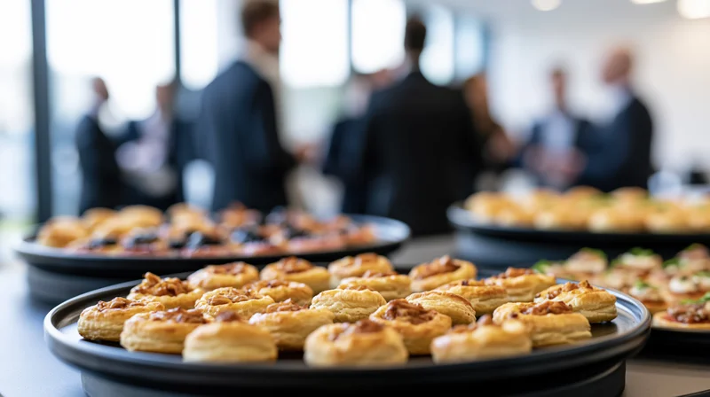 Golden puff pastry canapes on black trays at a corporate event buffet with professionals in suits in the background
