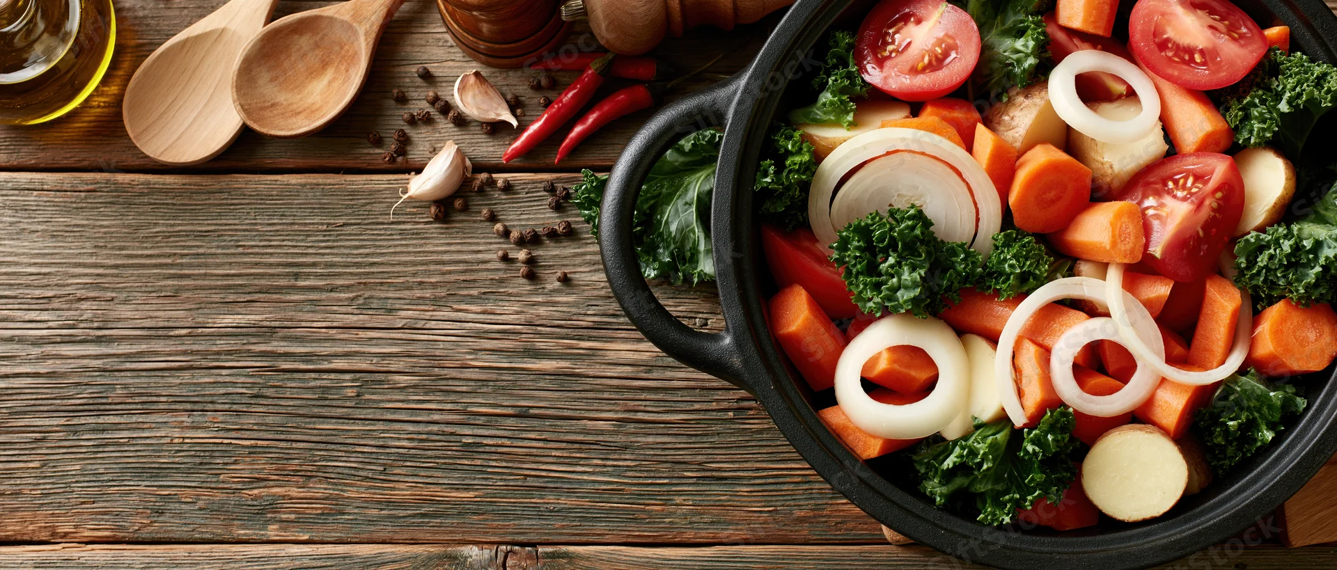 Cast iron pot filled with chopped raw vegetables on wooden table