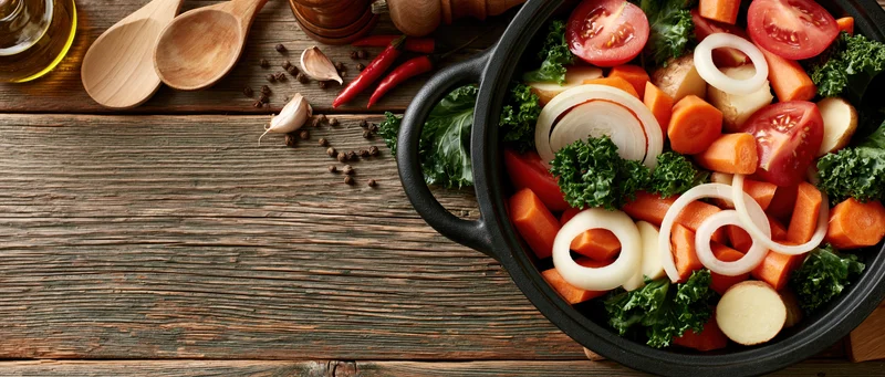 Cast iron pot filled with chopped raw vegetables on wooden table
