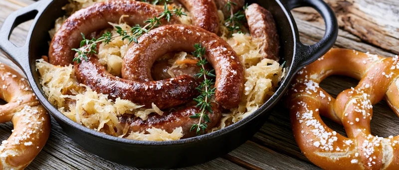 Bratwurst sausages with sauerkraut in a cast iron skillet served with pretzels on a wooden table