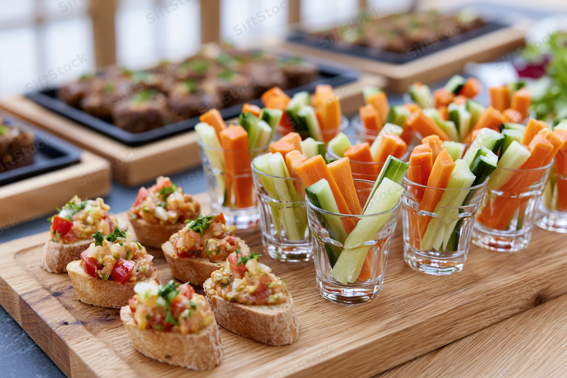 Canapes and crudite in shot glasses arranged on wooden boards for a catering event