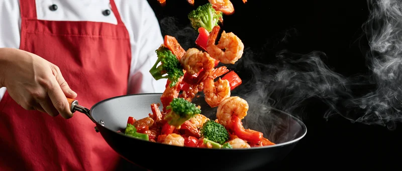 Chef tossing shrimp stir-fry with broccoli and red pepper in a wok