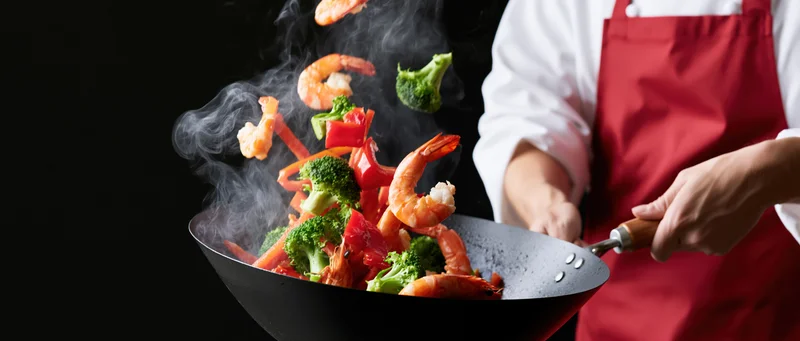 Chef tossing shrimp and vegetables in a wok with steam rising