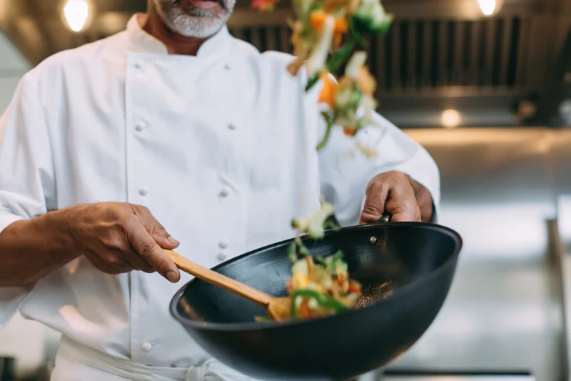Chef tossing colorful vegetables in a wok in a commercial kitchen
