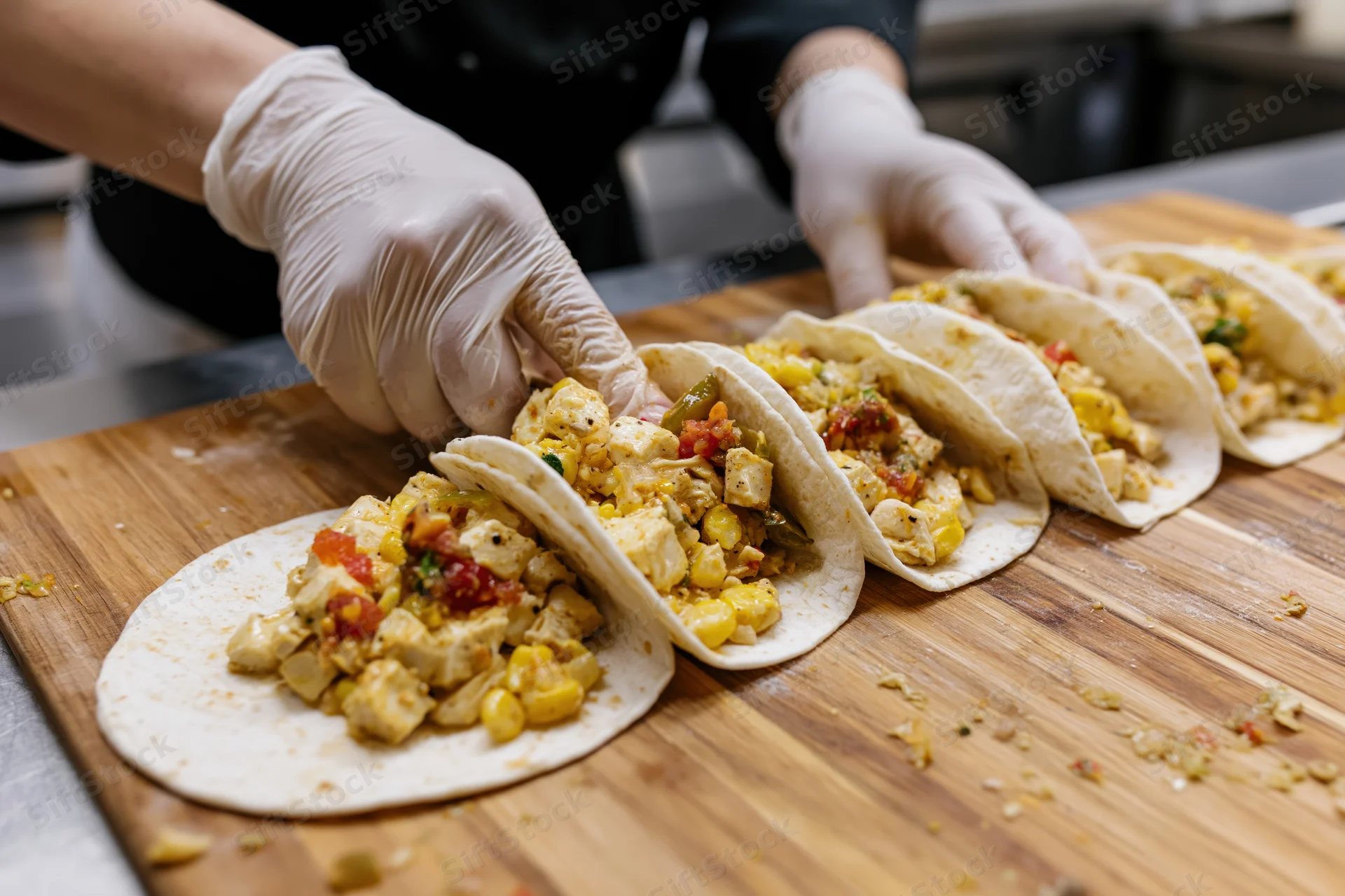 Chef assembling open-faced tacos with chicken and vegetables on a wooden cutting board