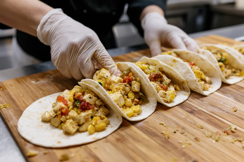 Chef assembling open-faced tacos with chicken and vegetables on a wooden cutting board