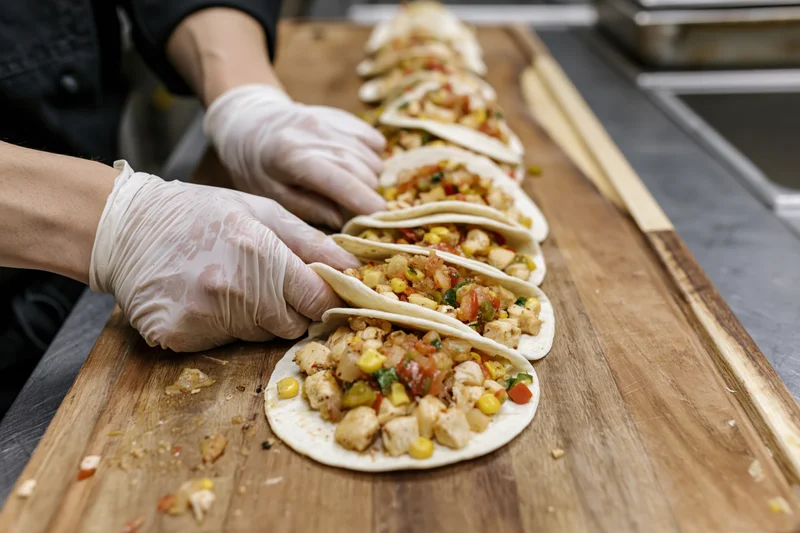 Chef assembling open-faced tacos in a row on a wooden cutting board