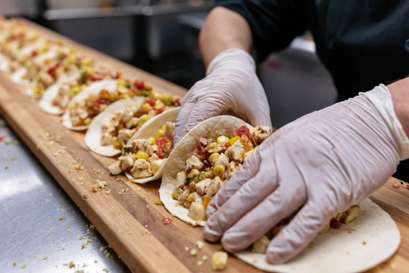 Chef assembling open-faced tacos with chicken and vegetables on a wooden board in a kitchen