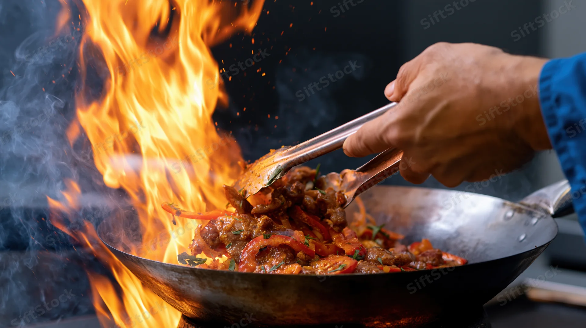 Chef’s hand using tongs to stir food in a flaming wok
