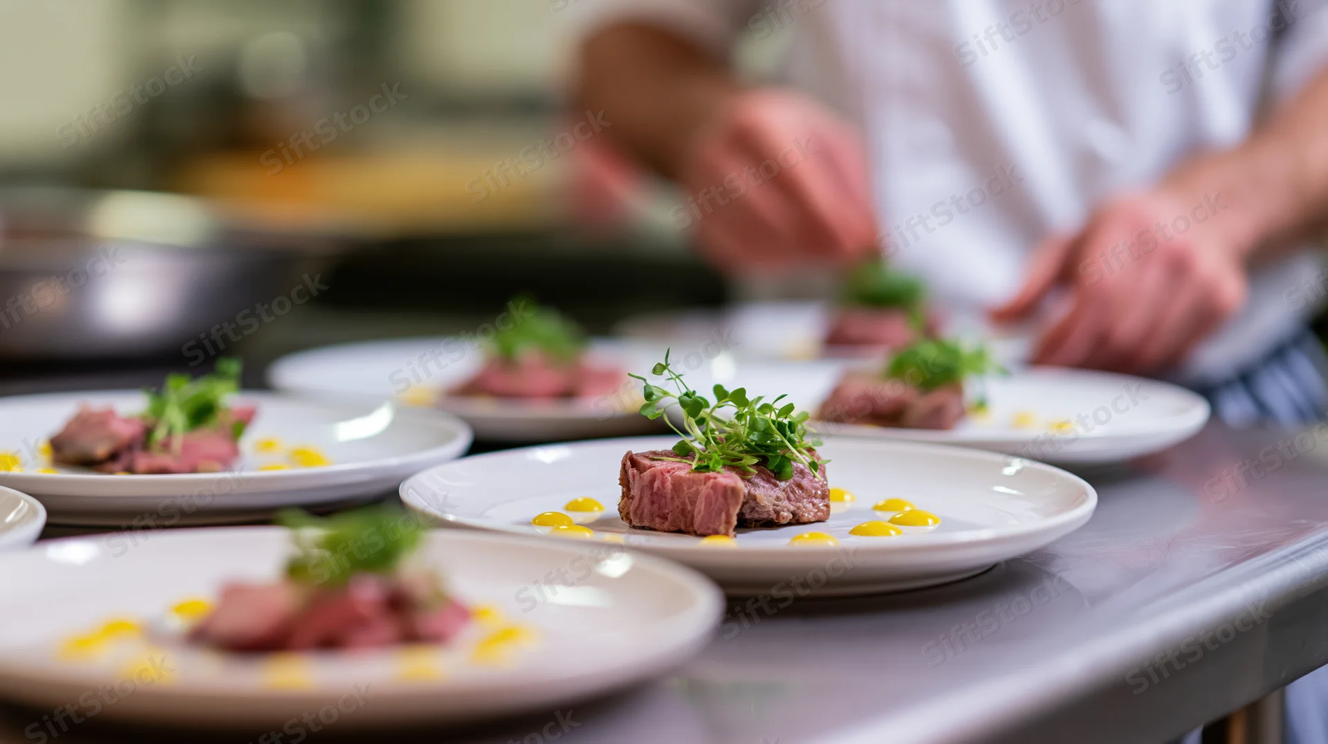 Chef plating gourmet steak dishes with microgreens and sauce on stainless steel counter
