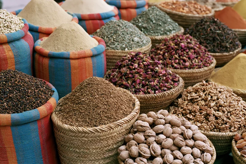 Various dried spices and herbs in woven baskets and colorful cloth containers arranged in a market display