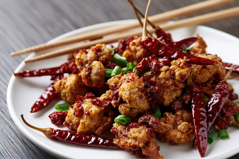 Crispy fried chicken pieces with dried red chilies and green onions on a white plate with chopsticks on a gray wooden table