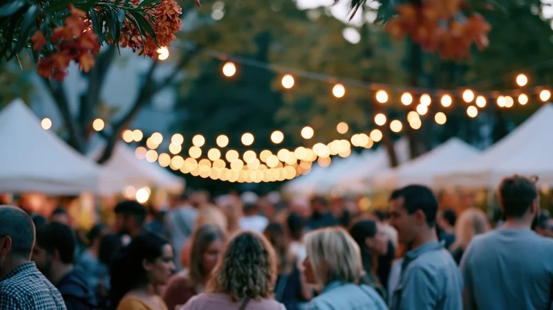 Crowd of people mingling at an outdoor evening festival under string lights and tents